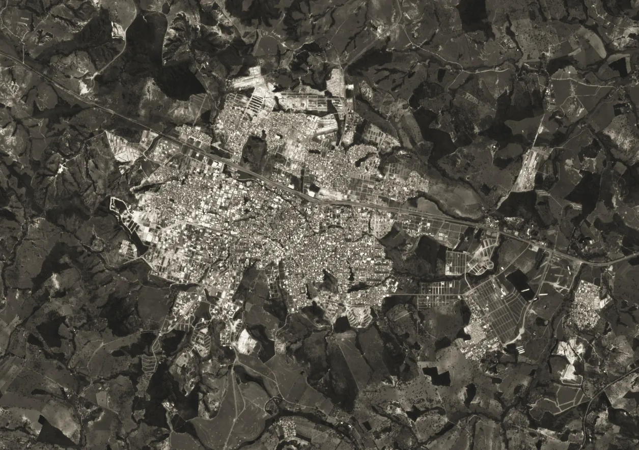 Two Sentinel-2 images of the same area in warm gray tones, from 2018 and from 2026: new subdivisions appear at the edges of the town on the more recent date